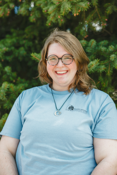 Smiling person with glasses outdoors by evergreen trees