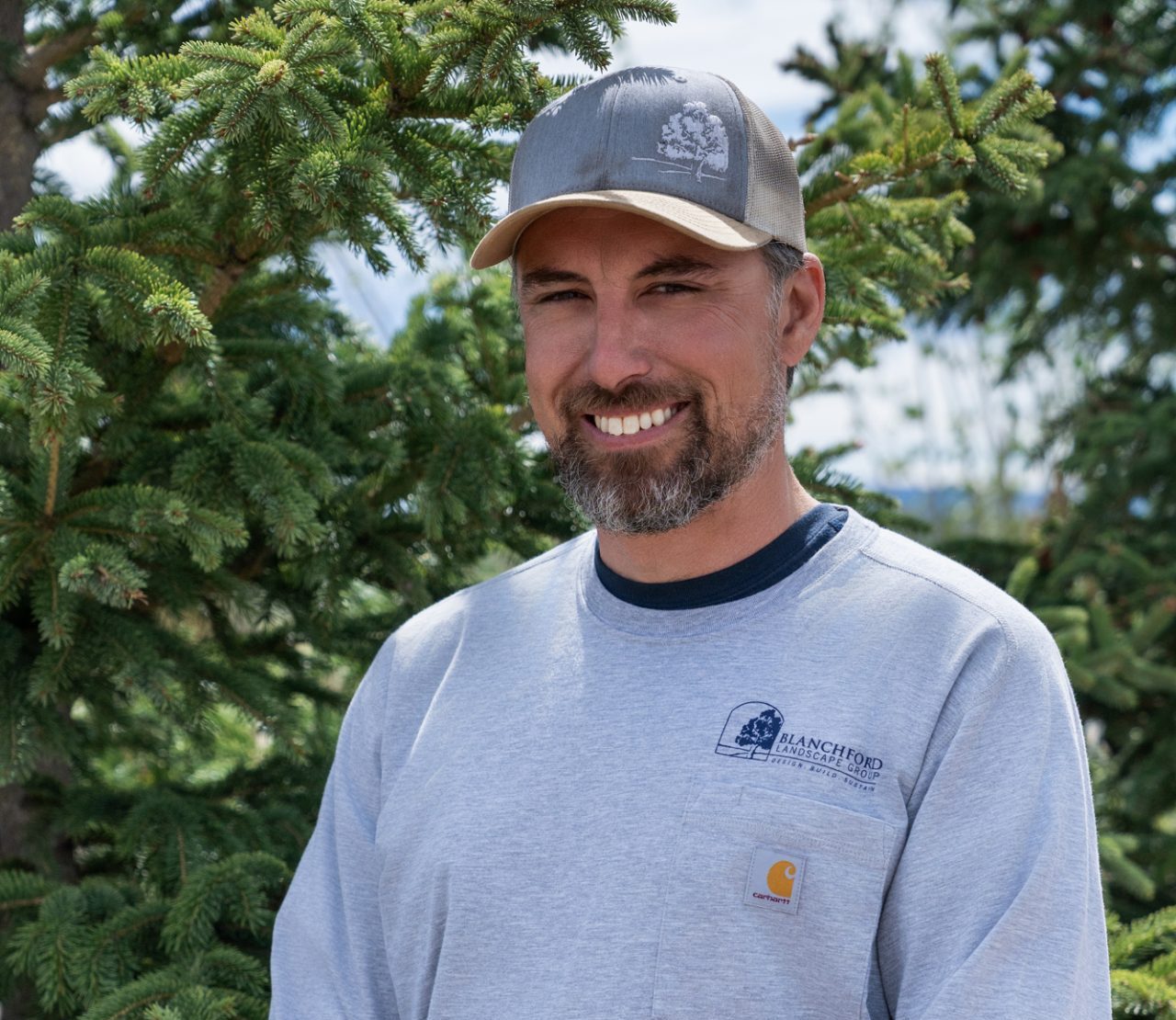 Smiling man in cap beside evergreen trees