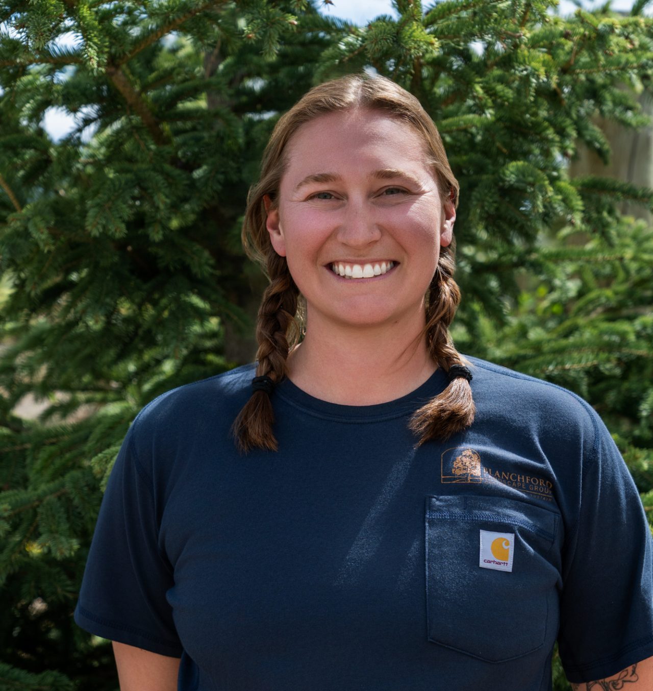 Smiling woman with braids standing before evergreen tree