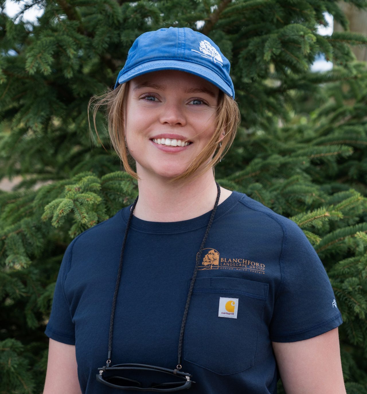 Smiling landscaper standing in front of evergreen trees