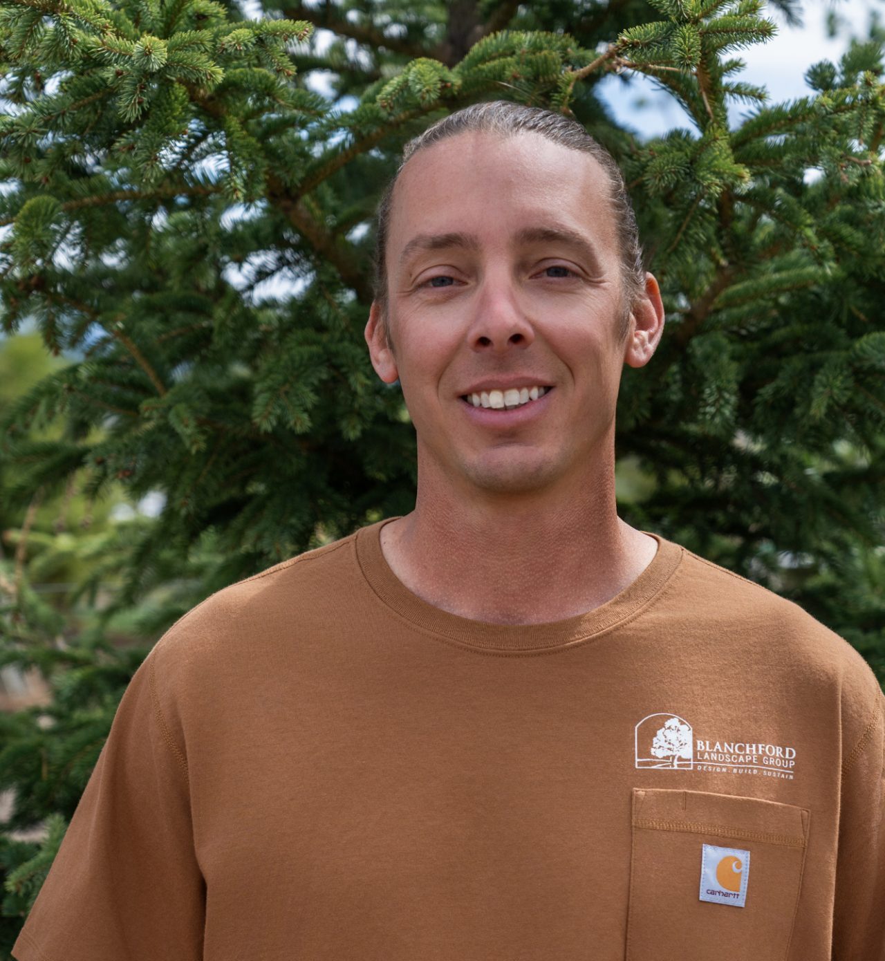 Man smiling outdoors in front of evergreen trees