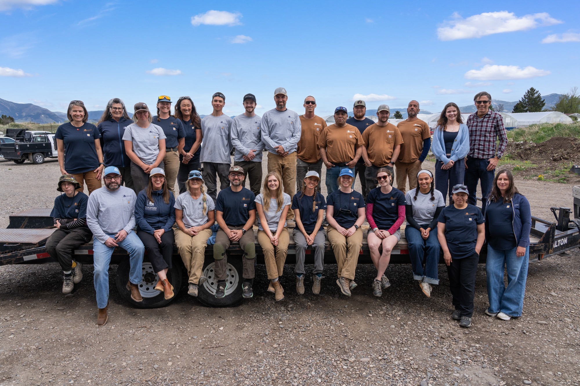 Team posing outdoors on farm trailer with mountains