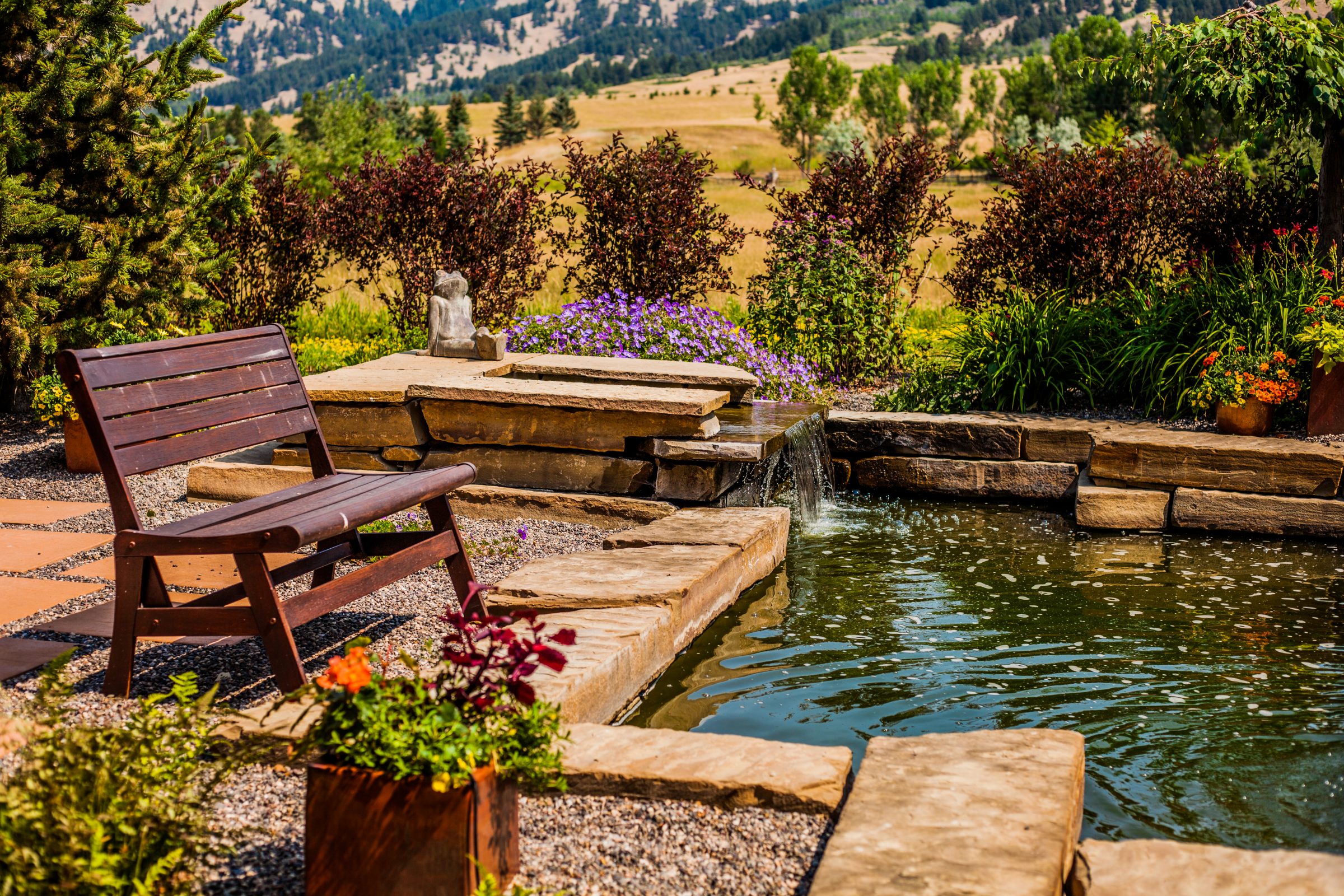 Wooden bench beside stone garden pond and waterfall