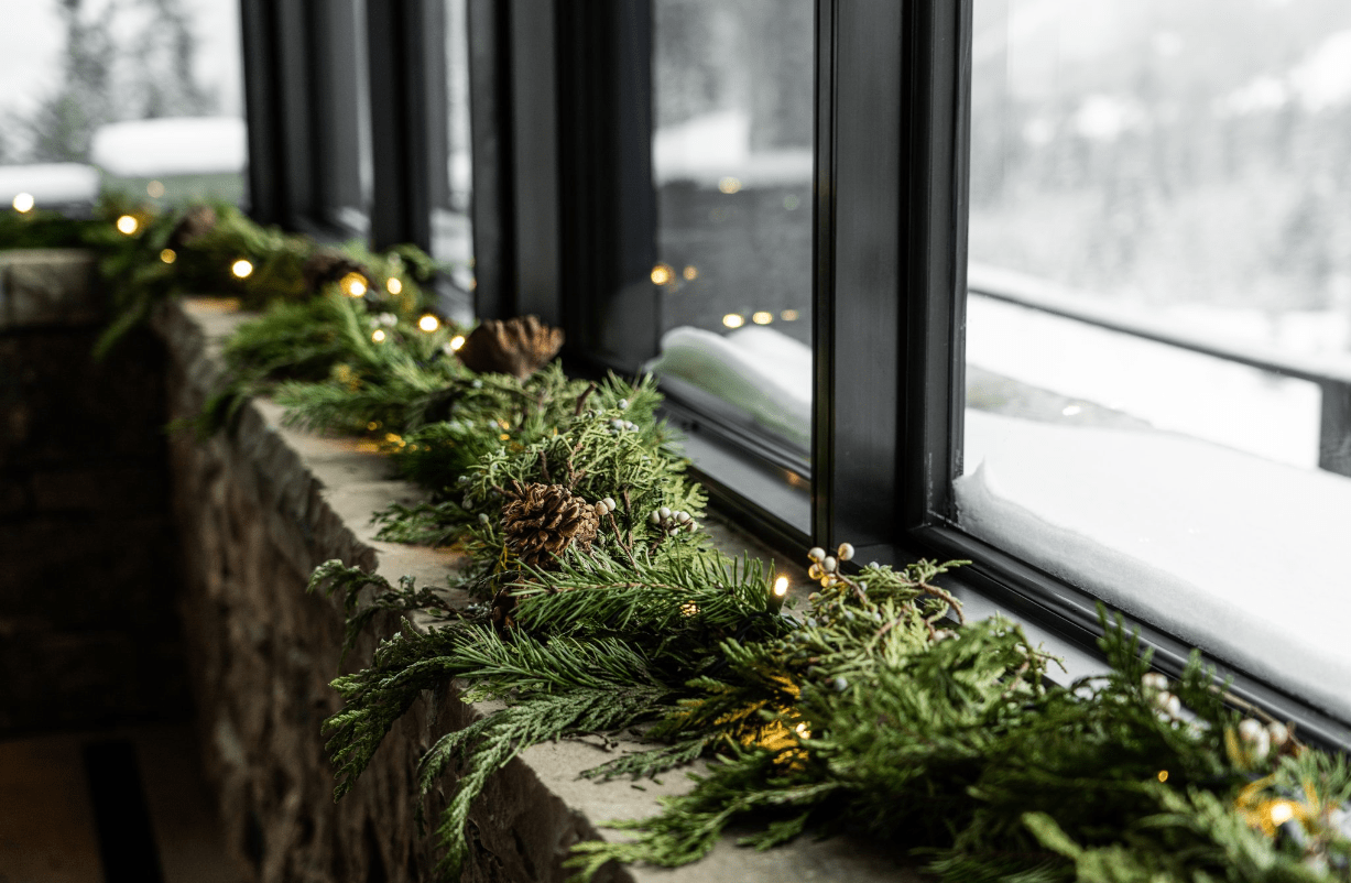 Evergreen garland with lights on snowy windowsill