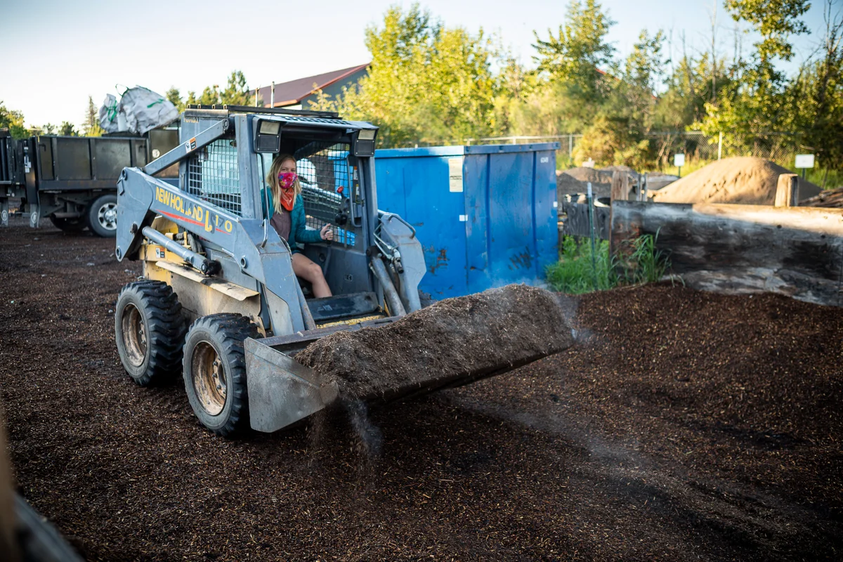 Person operating skid-steer loader moving mulch